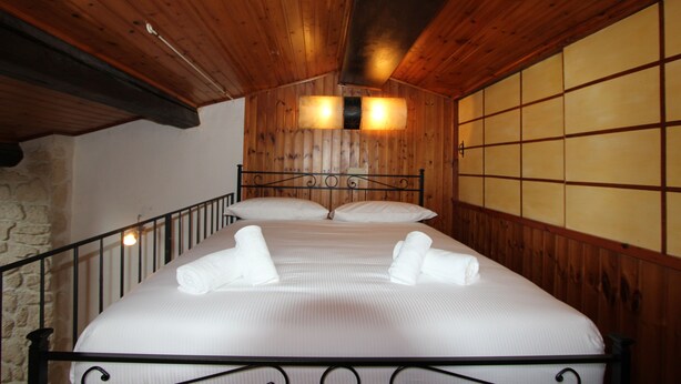 A neatly made bed with white linens and towels, a wooden ceiling, and a stone wall. - Oltrarno Loft (Florence)