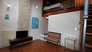 A living room with a stone wall, a wooden bench, a TV stand, and a metal cart. - Oltrarno Loft (Florence)