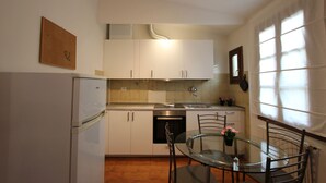 A compact kitchen with white cabinets, a built-in oven, a refrigerator, and a glass dining table with chairs. - Oltrarno Loft (Florence)