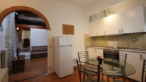 A compact kitchen with white cabinets, a glass table, and a refrigerator. - Oltrarno Loft (Florence)