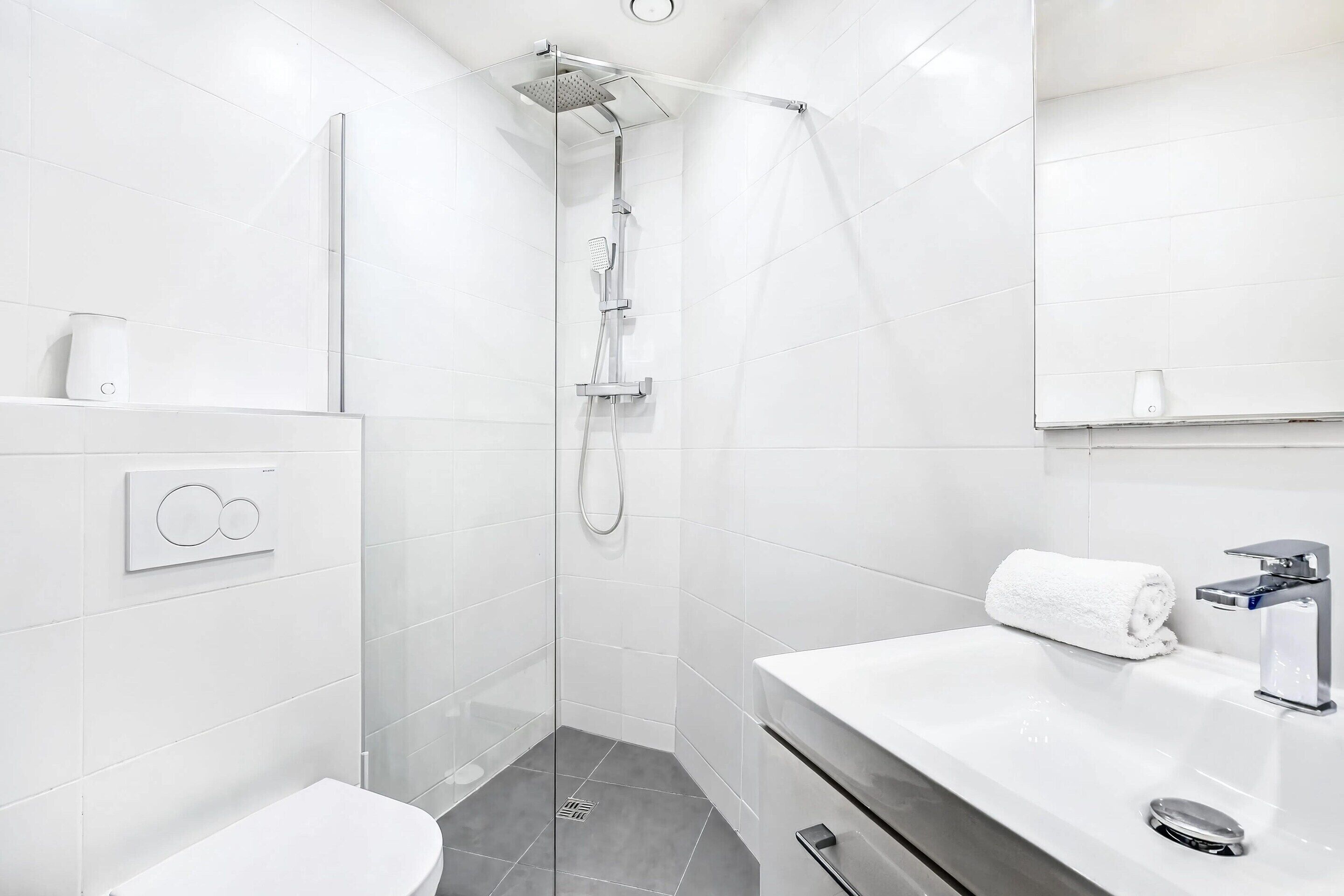 Un baño moderno con ducha envuelta en vidrio, lavamanos blanco y un espejo sobre el mueble.