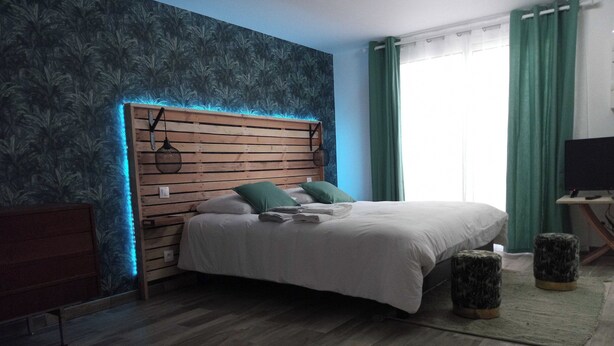 Une chambre à coucher avec une tête de lit en bois, un lit avec une literie blanche, des oreillers verts et une petite table de chevet.