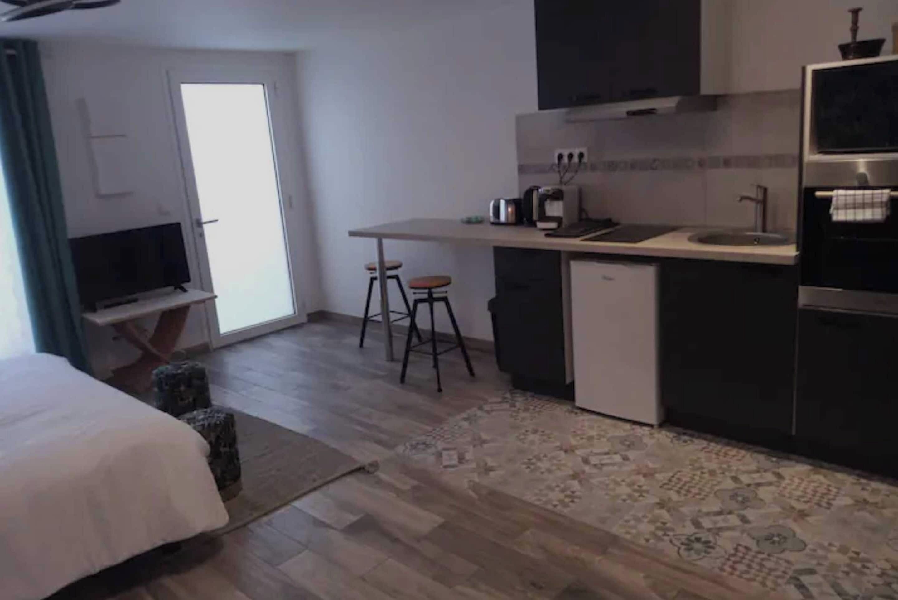 Ett kompakt hotellrum med en säng, ett litet pentry, en tv och en dörr som leder ut till en balkong.