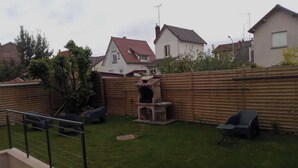 Un jardin avec une clôture en bois, un barbecue et un petit espace patio équipé d’une chaise.