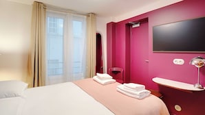 A hotel room with a bed, a bedside table, a TV mounted on the wall, and a window with curtains. - Intimate Studio - 2P - Republique (Paris)