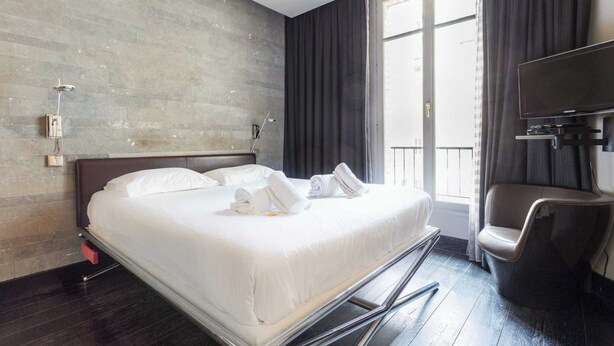 Une chambre d’hôtel avec un grand lit, une télévision, une chaise et une fenêtre avec des rideaux.
