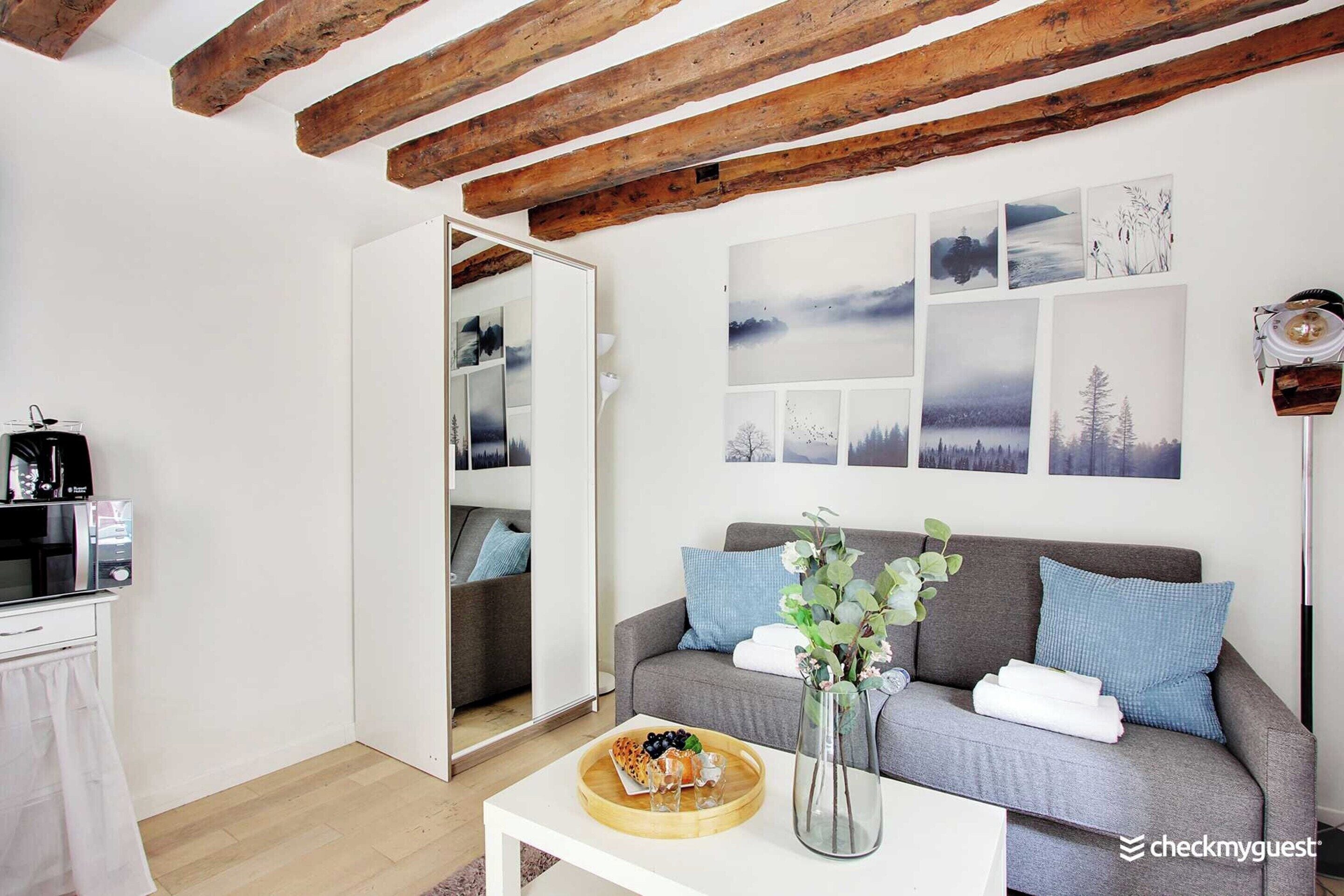 A modern living room with a grey sofa, wooden beams, and a coffee machine.