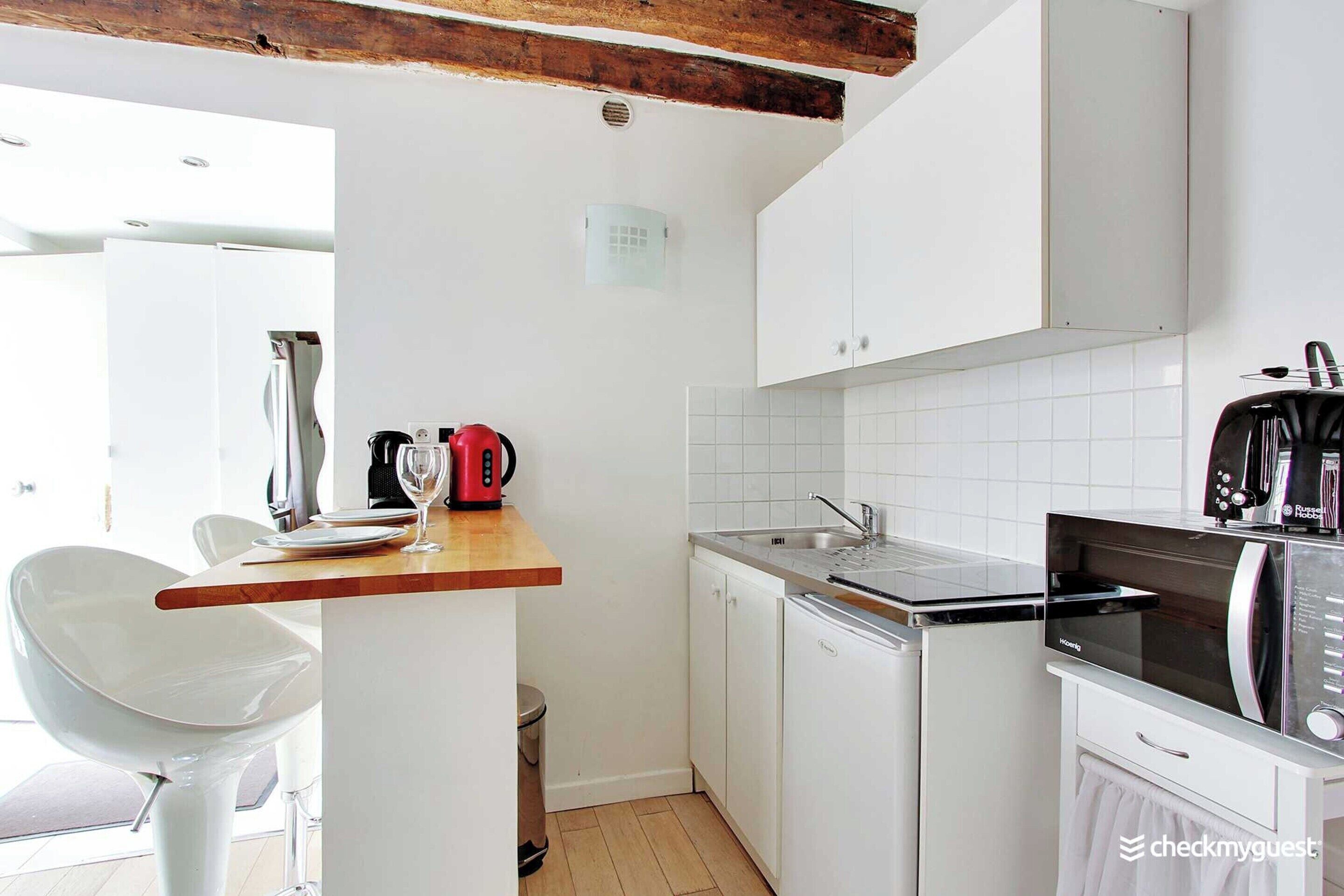 A compact kitchen with white cabinets, a microwave, a coffee maker, and a sink.