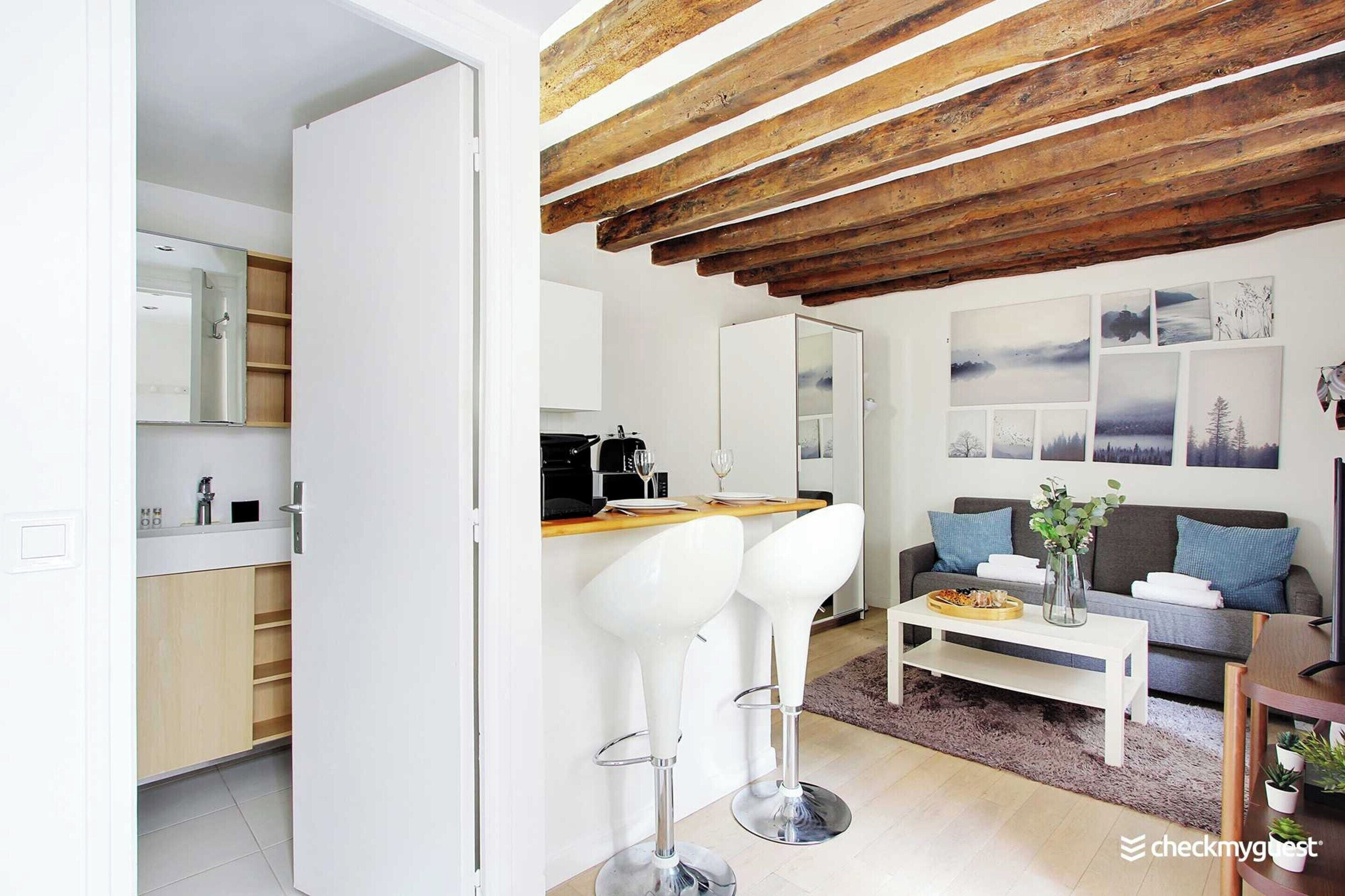 Uma sala de estar moderna com teto de madeira, um sofá, uma mesa de centro e uma área de cozinha com banquetas.