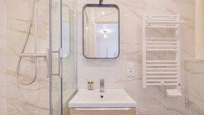 A modern bathroom with a glass shower enclosure, a white sink with a mirror above it, and a towel rack. - Cosy Studio for 2P - Le Bon Marche (Paris)