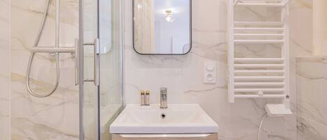 Een moderne badkamer met een douchecabine van glas, een witte wastafel met spiegel erboven en een handdoekrek.
