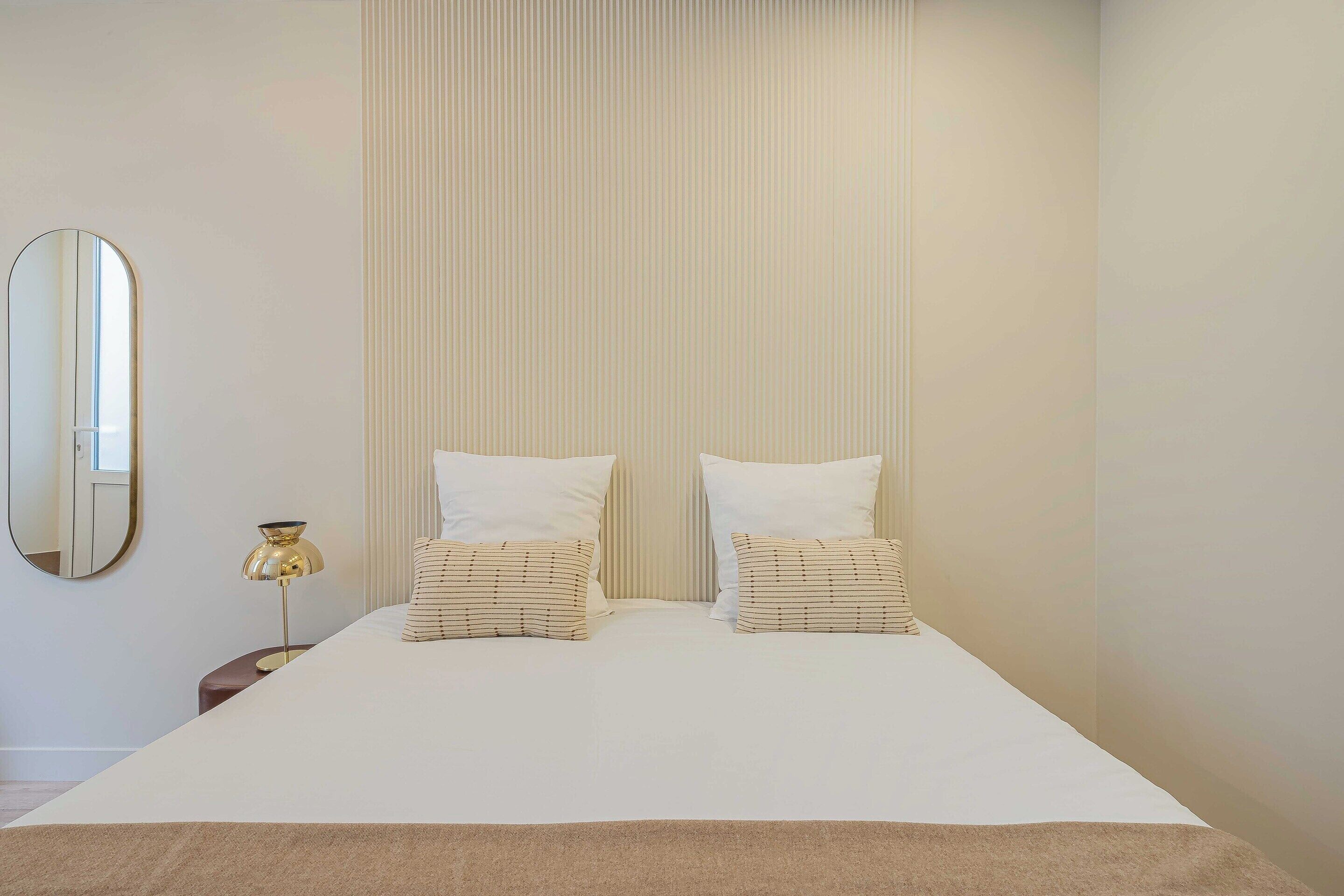 A neatly made bed with two pillows, a bedside lamp, and a mirror on the wall.