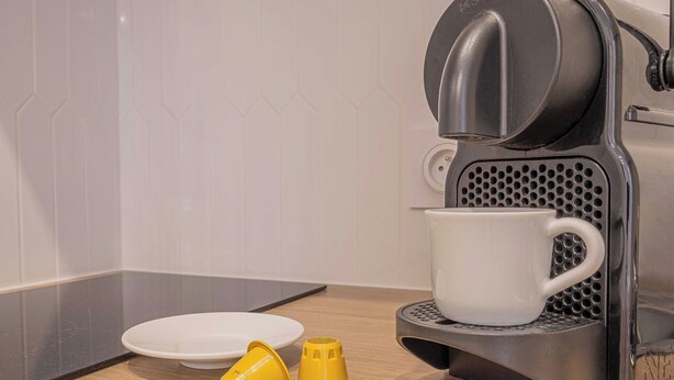 A coffee maker with a white mug on its drip tray, a white plate, and two yellow coffee filters on a wooden countertop. - Cosy Studio for 2P - Le Bon Marche (Paris)