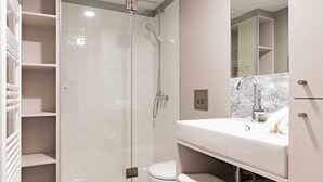 Un baño moderno con cabina de ducha de vidrio, suelo de mármol y tocador blanco con un espejo grande.