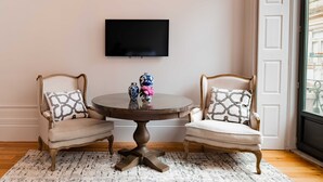 Una habitación con dos sillones, una mesa redonda con jarrones decorativos y un televisor de pantalla plana montado en la pared.