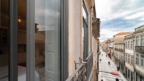 Una calle estrecha flanqueada por edificios, con un balcón de barandilla de hierro forjado y algunas personas caminando.