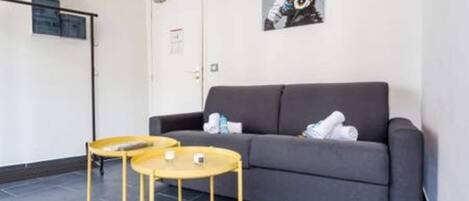 A modern room with a grey sofa, two small round tables, and a framed picture on the wall.