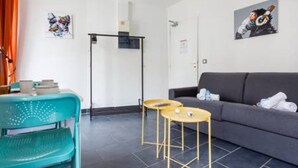 A modern living room with a grey sofa, teal chair, and two small round tables. - Magnificent Studio - 2P - Pantin (Pantin)
