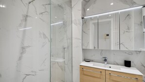 A modern bathroom with a glass shower enclosure, a marble-tiled wall, a wooden vanity with a sink, and a large mirror above the vanity. - Studio 2p - Avenue Foch (Paris)