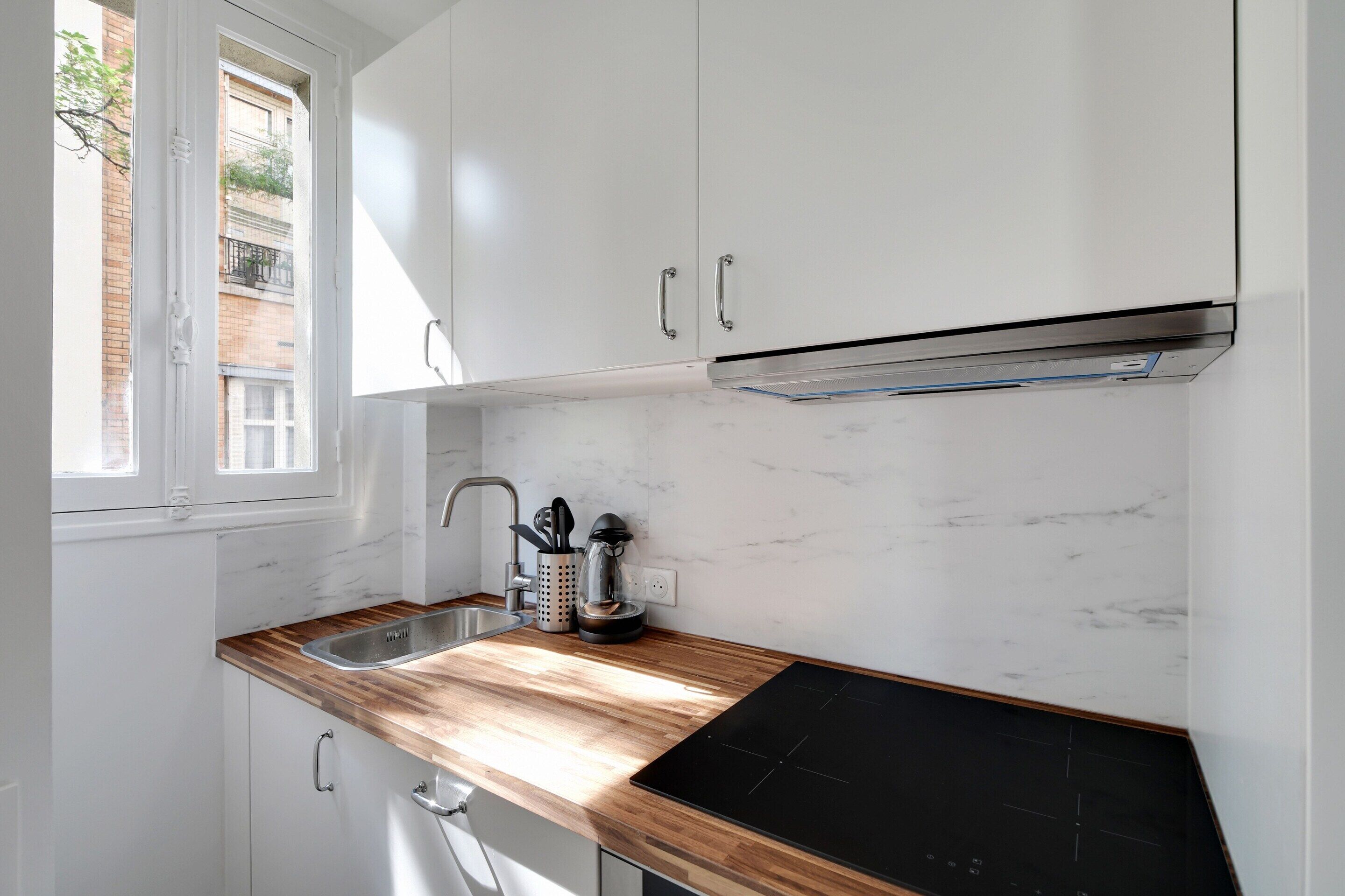 A kitchen with white cabinets, a wooden countertop, a black stove top, and a window with a view of a building outside.