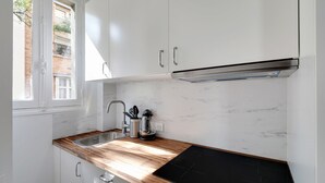 A kitchen with white cabinets, a wooden countertop, a black stove top, and a window with a view of a building outside. - Studio 2p - Avenue Foch (Paris)