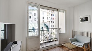 A modern apartment with a balcony, a TV, a sofa, and a framed picture on the wall. - Studio 2p - Avenue Foch (Paris)