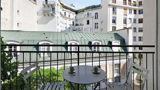 A balcony with a table and two cups, overlooking a courtyard with buildings and a green roof. - Studio 2p - Avenue Foch (Paris)