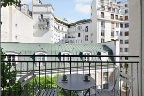 Un balcón con una mesa y dos tazas, con vistas a un patio que incluye edificios y un techo verde.