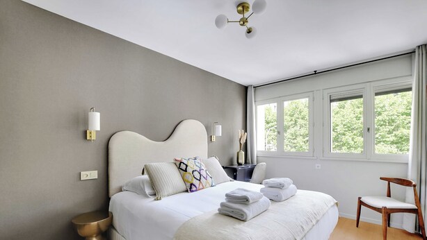 A modern bedroom with a large bed, bedside lamps, a wooden floor, and a view of greenery through the windows. - Modern "green Suites" Residence - Meudon/velizy (Meudon)