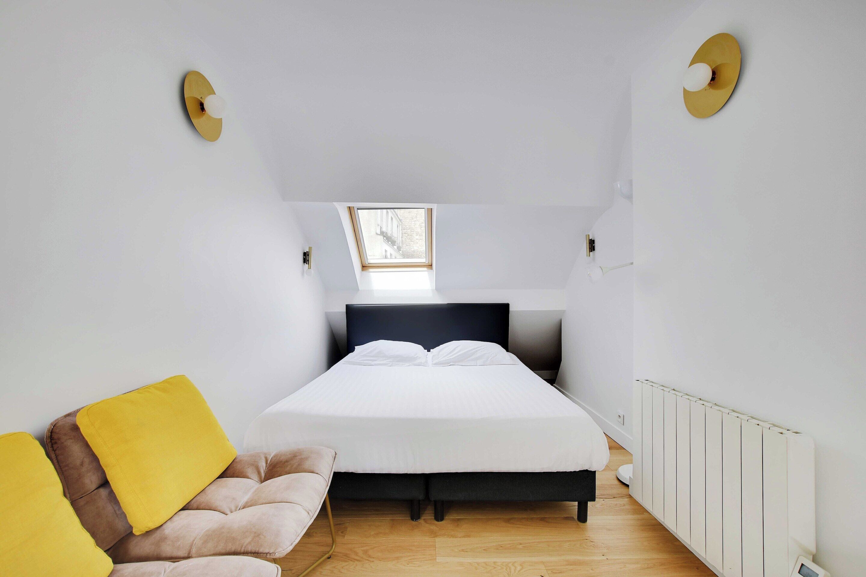 A bedroom with a bed, a window, a radiator, and a couch.