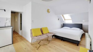 A modern bedroom with a bed, a desk, and a chair with yellow cushions. - Charming Studio for 2 People - Bastille (Paris)