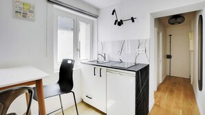 A modern kitchen with white cabinets, a black countertop, and a black chair. - Charming Studio for 2 People - Bastille (Paris)
