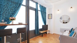 Moderni olohuone, jossa on ruokailutila. Tilan ominaisuuksiin kuuluu kalanruotokuviollinen puulattia, pyöreä peili ja sohva, jonka päällä on pyyhkeitä.