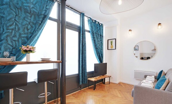 Una sala de estar moderna con comedor, que presenta piso de madera en espiga, un espejo redondo y un sofá con toallas.