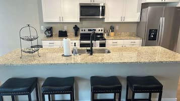 Una cocina moderna con armarios blancos, encimera de granito, refrigerador de acero inoxidable y horno empotrado.