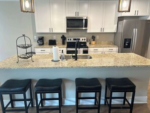 A modern kitchen with white cabinets, a granite countertop, a stainless steel refrigerator, and a built-in oven. - Spacious 8BR 8BA Combined Condos in Traverse City (Williamsburg)