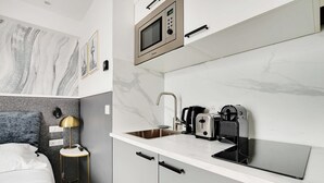 Ett kompakt hotellrum med en säng, ett sängbord, en lampa och ett litet kök med mikrovågsugn, brödrost och kaffebryggare.