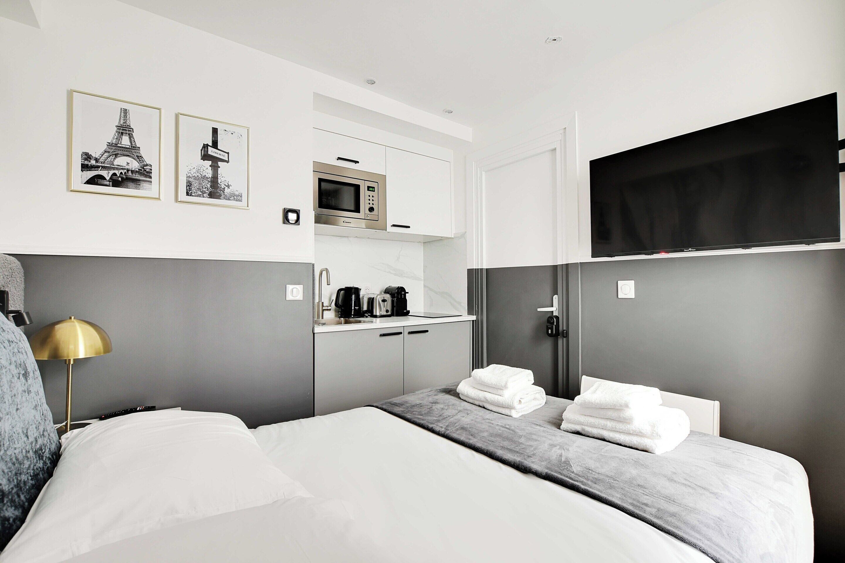 Habitación de hotel con cama, mesita de noche, lámpara, microondas, televisión y dos cuadros en la pared.