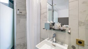 A modern bathroom with a glass shower enclosure, a white sink with a chrome faucet, and a mirror above the sink. - Hotel Avaton - Deluxe Balcony Bedroom - Cannes Palais (Cannes)