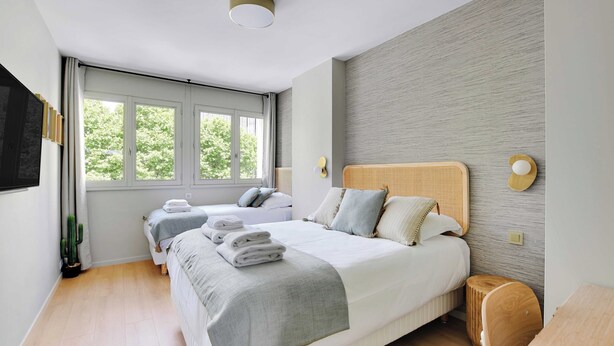 A modern bedroom with a large bed, two smaller beds, a wooden floor, and a window with a view of greenery. - Modern "green Suites" Residence - Meudon/velizy (Meudon)