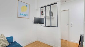 Una habitación moderna con un sofá azul, un televisor de pantalla plana montado en la pared y una puerta que da a una zona de cocina.