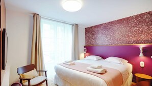 A modern hotel room with a large bed, a chair, a small table, and a wall-mounted light fixture. - Charming Studio - 2P - Republique/oberkampf (Paris)
