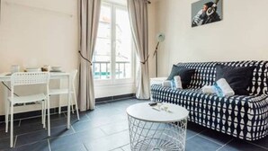 Ein gemütlicher Wohnbereich mit einem gemusterten Sofa, einem kleinen runden Tisch und einem weißen Stuhl.