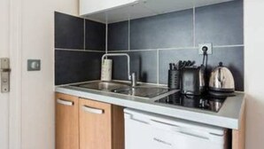 Eine kompakte Küche mit integriertem Geschirrspüler, Spüle aus Edelstahl und Wasserkocher auf der Arbeitsplatte.