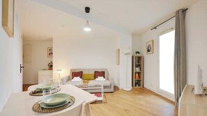 Ein modernes Wohnzimmer mit Essbereich, einer Couch, einem Bücherregal und einem großen Fenster mit Vorhängen.