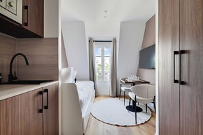 A compact hotel room with a kitchenette, a bed, a dining area, and a large window. - Bright and Modern Studio - 2P - Passy (Paris)