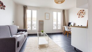 Een moderne woonkamer met een grijze bank, een glazen salontafel en een hanglamp van riet.
