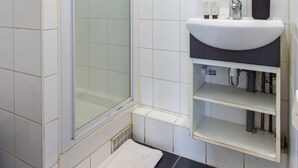Een badkamer met een douchecabine van glas, een witte wastafel met een donker aanrechtblad en een spiegel boven de wastafel.