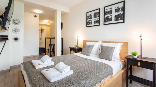 A modern hotel room with a large bed, a bedside table with a lamp, and a wall-mounted TV. - Magnificent Studio - 2P - Moulin Rouge (Paris)