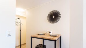 A small dining area with a wooden table, black stools, a wall-mounted decorative piece, and a coat rack. - Magnificent Studio - 2P - Moulin Rouge (Paris)